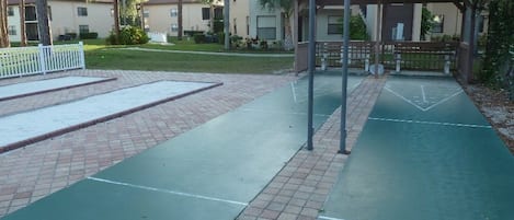 A tennis court with a pavilion, a brick pathway, and a building in the background.