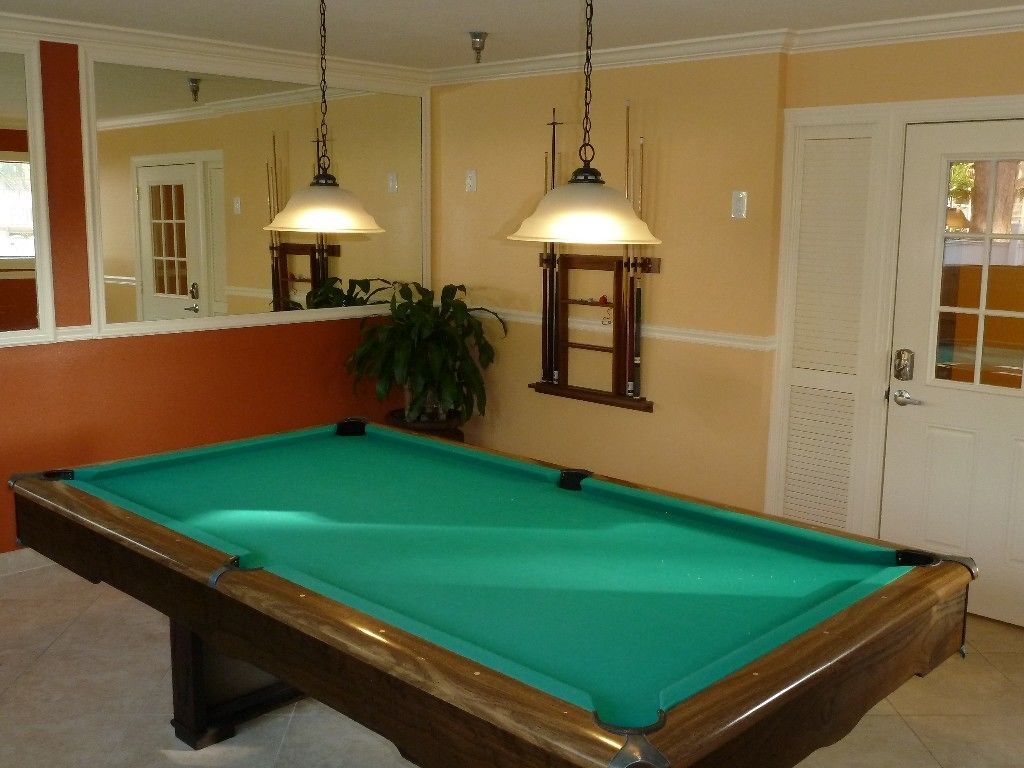 A pool table with two hanging lamps, a potted plant, and a door with a window in the background.