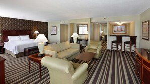 Habitación de hotel con cama, dos sillones, un sofá, una mesa de centro, un televisor y un escritorio con lámpara.