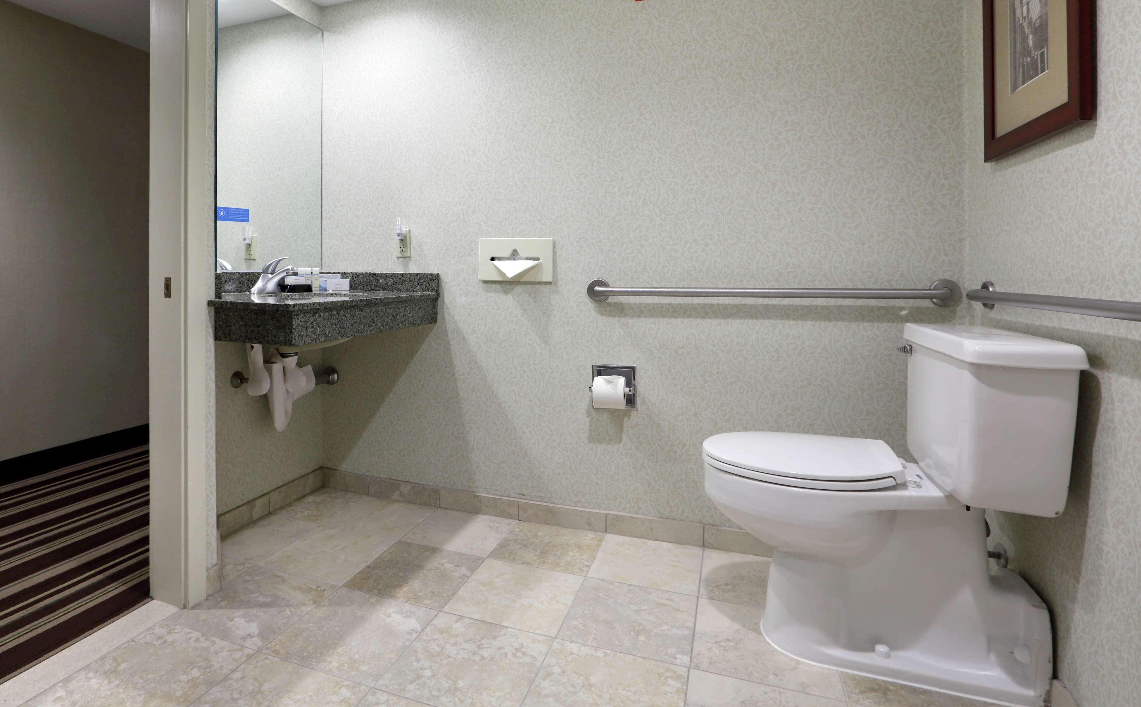 A bathroom with a toilet, a sink with a towel dispenser, and a handrail.