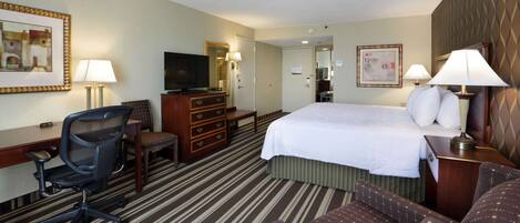 Habitación de hotel con cama, escritorio, silla, cómoda, televisor y lámparas.