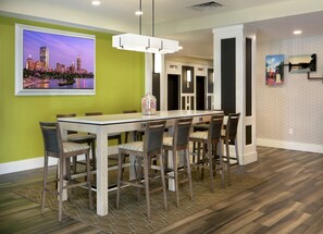 A modern dining area with a long table and chairs, a cityscape painting on the wall, and a patterned rug.