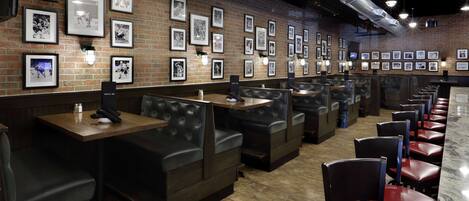 A restaurant with brick walls, framed pictures, leather booths, and a counter.