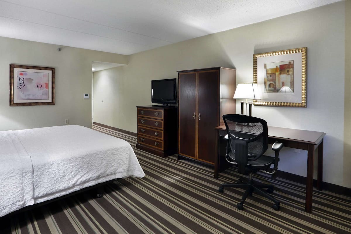 A hotel room with a bed, a desk, a chair, a TV, and a wardrobe.