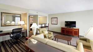 Habitación de hotel con sofá, sillón, escritorio, silla, televisor y espejo.