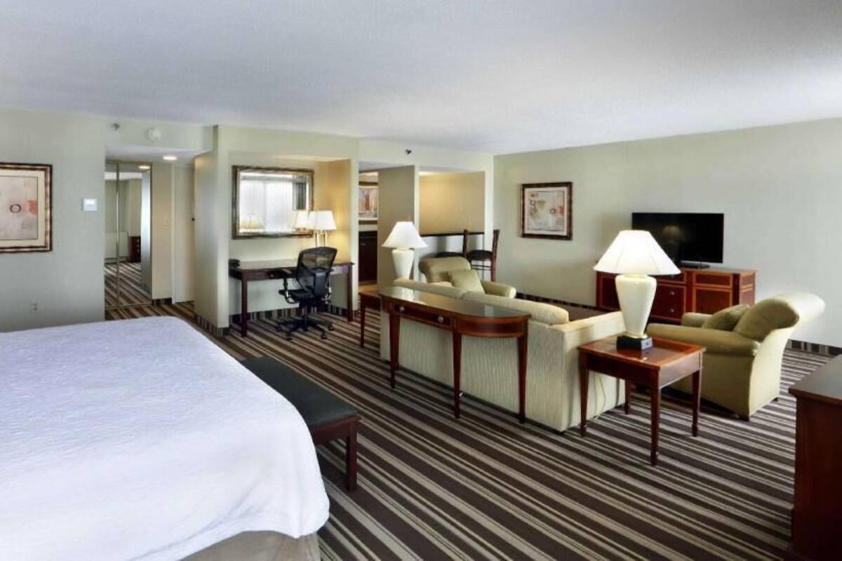 A hotel room with a large bed, a sofa, a desk, and a television.