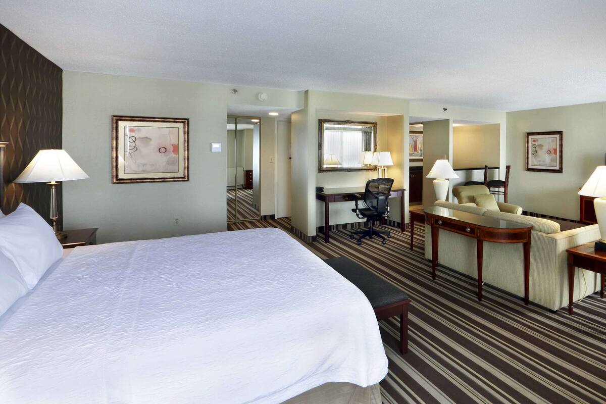 A hotel room with a large bed, a sofa, a desk, and a television.