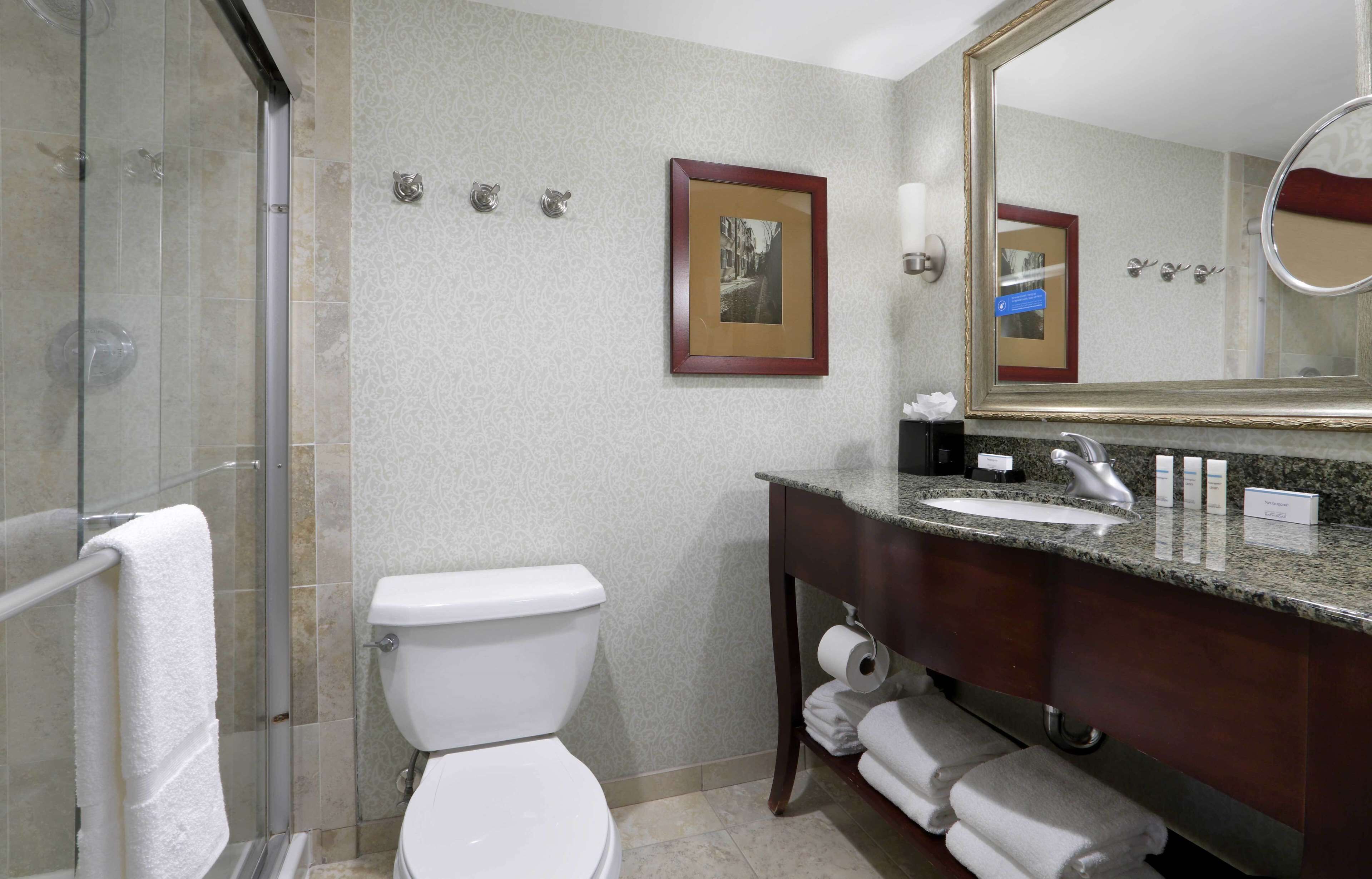 A bathroom with a glass shower enclosure, a white toilet, a sink with a marble countertop, and a mirror with a wooden frame.