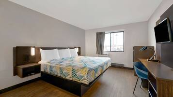 A hotel room with a bed, bedside table, TV, desk, chair, and a window with curtains.