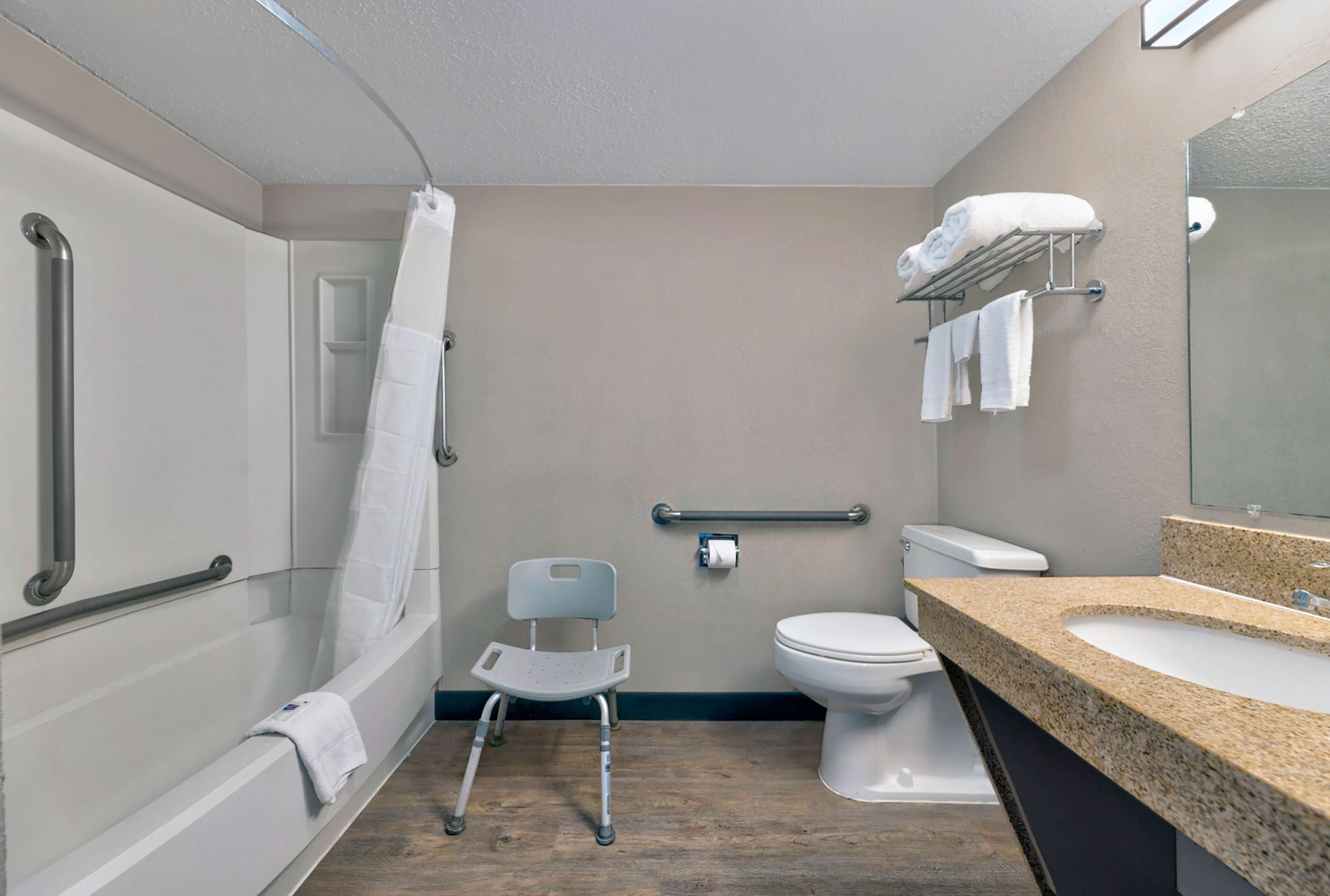 Et badeværelse med bruser, toilet, gelænder, en kørselssæde og en vask med granitbordplade.