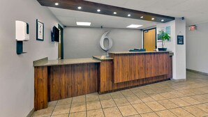 A reception area with a wooden reception desk, a framed certificate, a wall-mounted sign, and a potted plant.