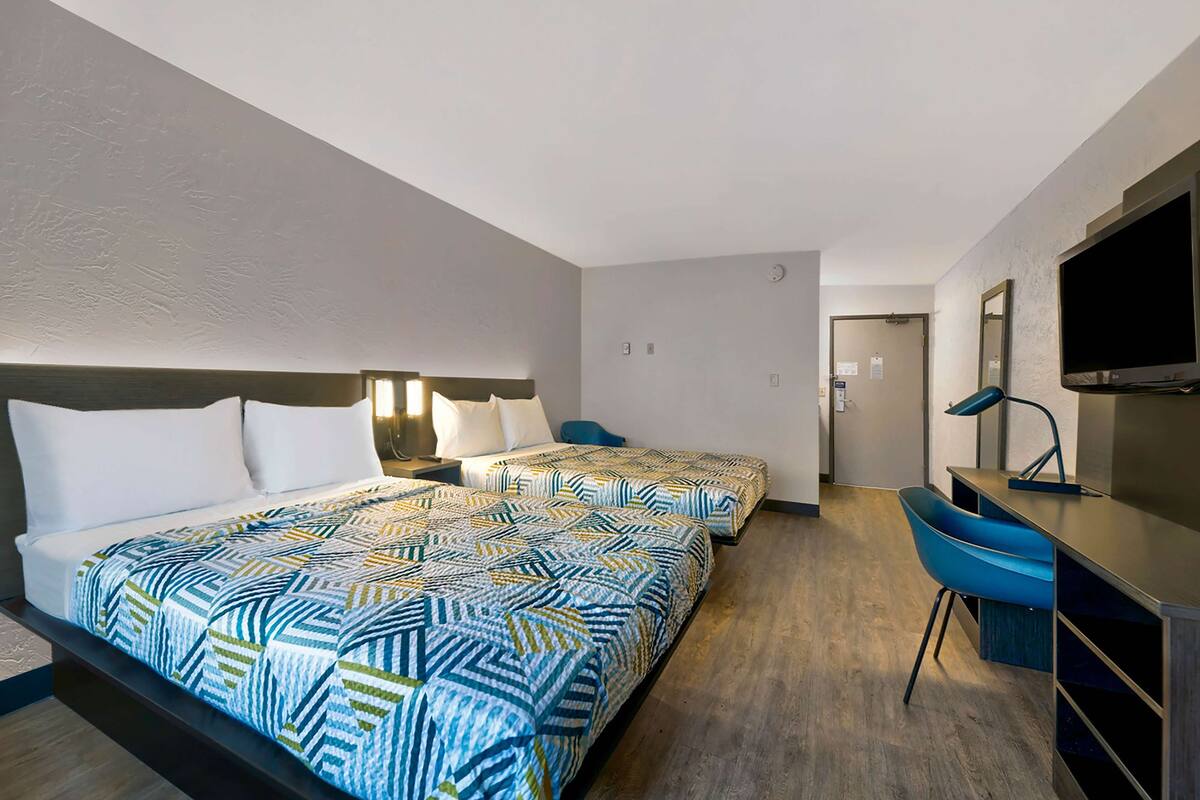 A hotel room with two beds, a desk, a chair, a TV, and a mirror.
