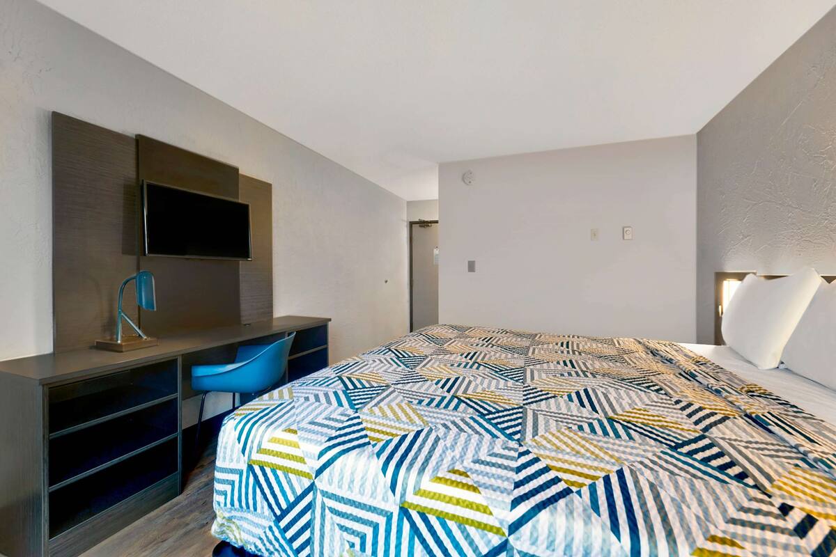 A modern hotel room with a bed, a desk with a chair, a flat-screen TV, and a large window.