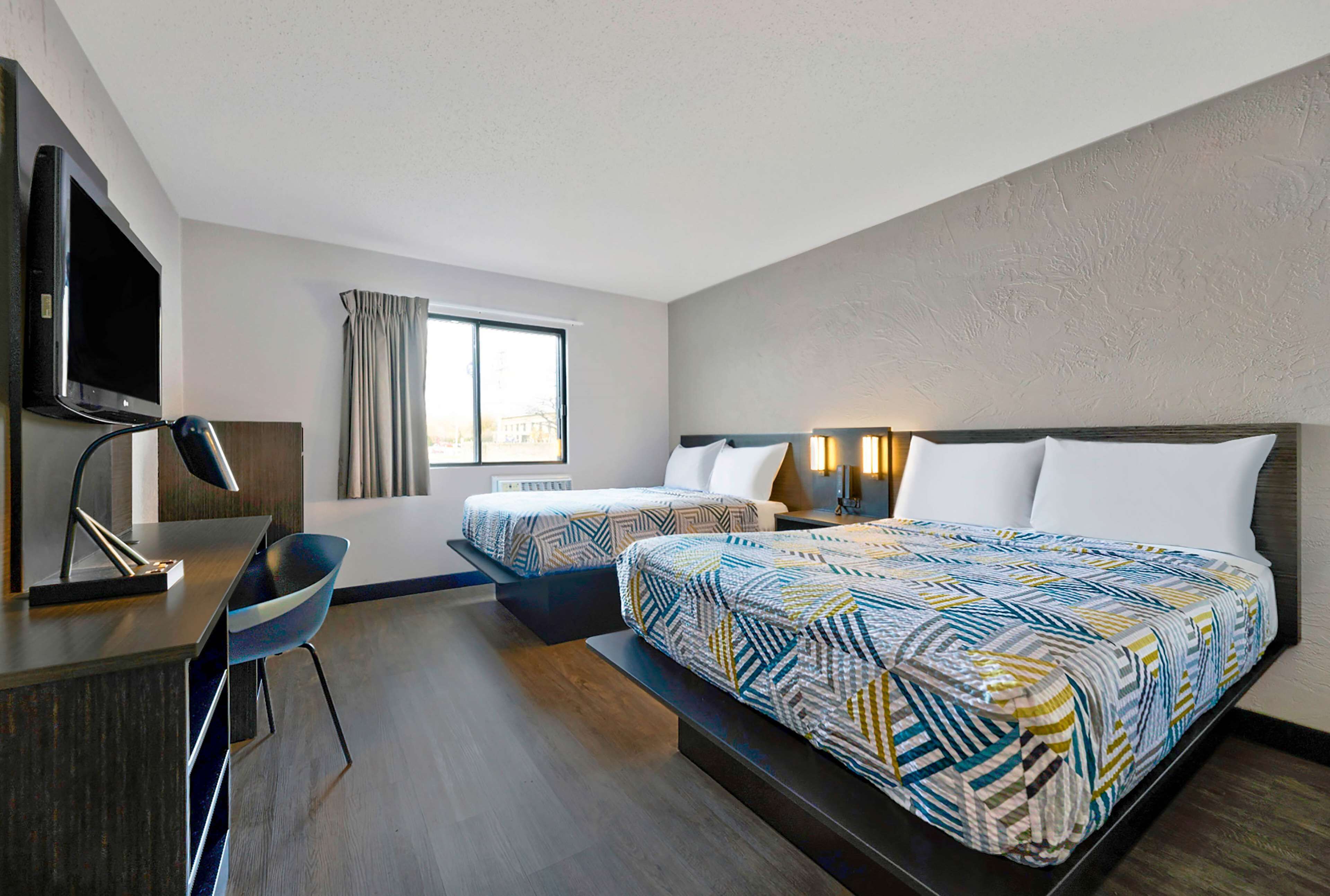 A hotel room with two beds, a desk, a chair, a TV, and a window with curtains.