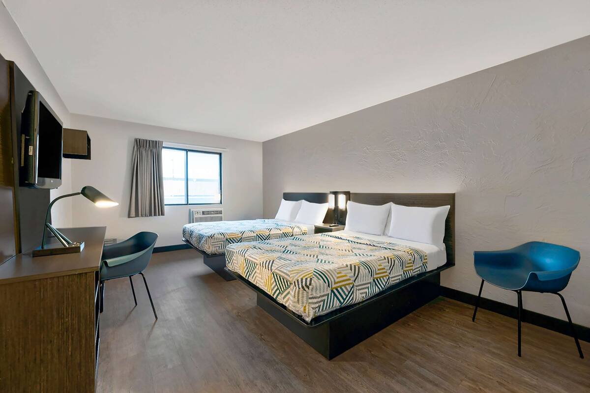 A hotel room with two beds, a desk, a chair, a TV, and a window with curtains.