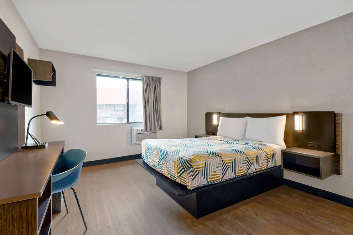 A hotel room with a bed, desk, chair, and a window with curtains.