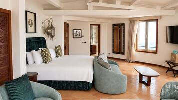 A spacious bedroom with a large bed, two sofas, a TV, and a view of the sea.