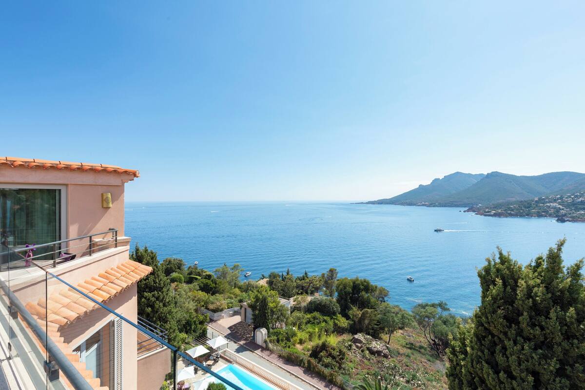 Un edificio costero con piscina, con vista al mar azul cristalino y montañas distantes.