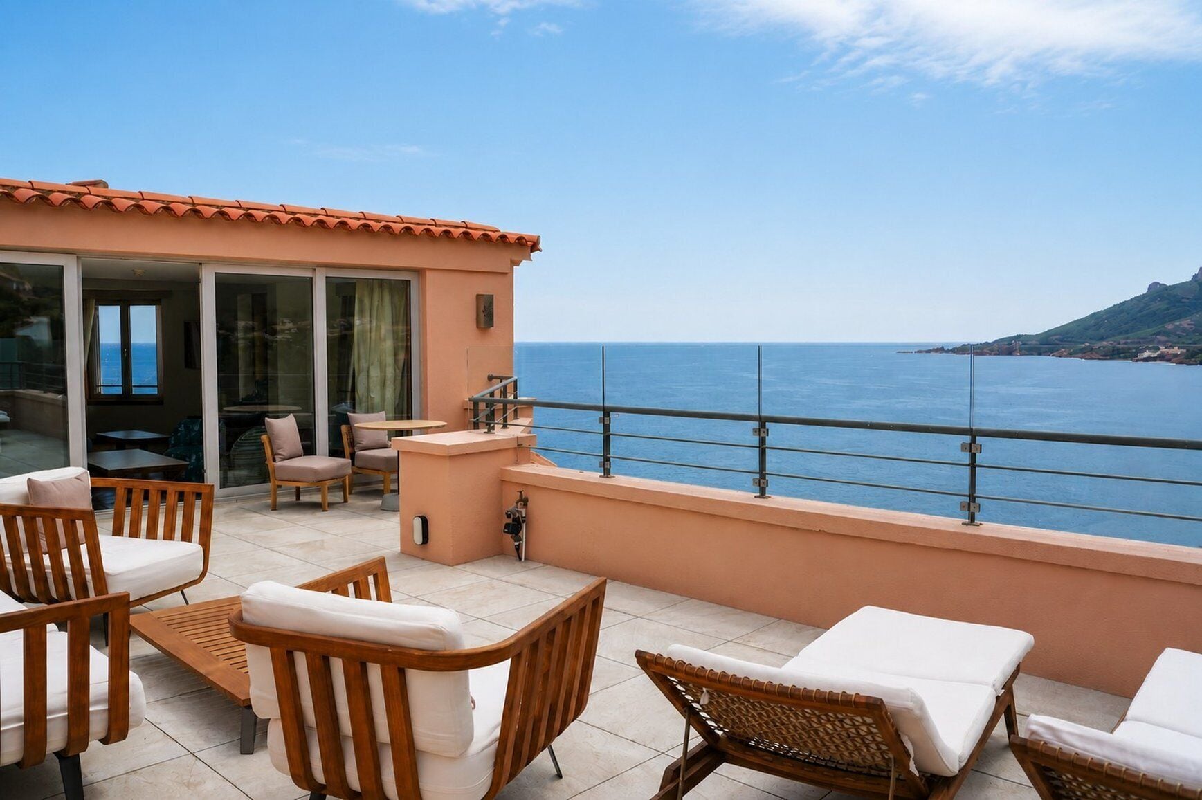 A terrace with outdoor furniture, a glass door leading to an interior space, and a view of the sea.