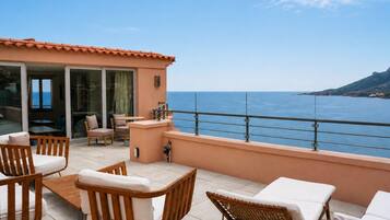 A terrace with outdoor furniture, a glass door leading to an interior space, and a view of the sea.