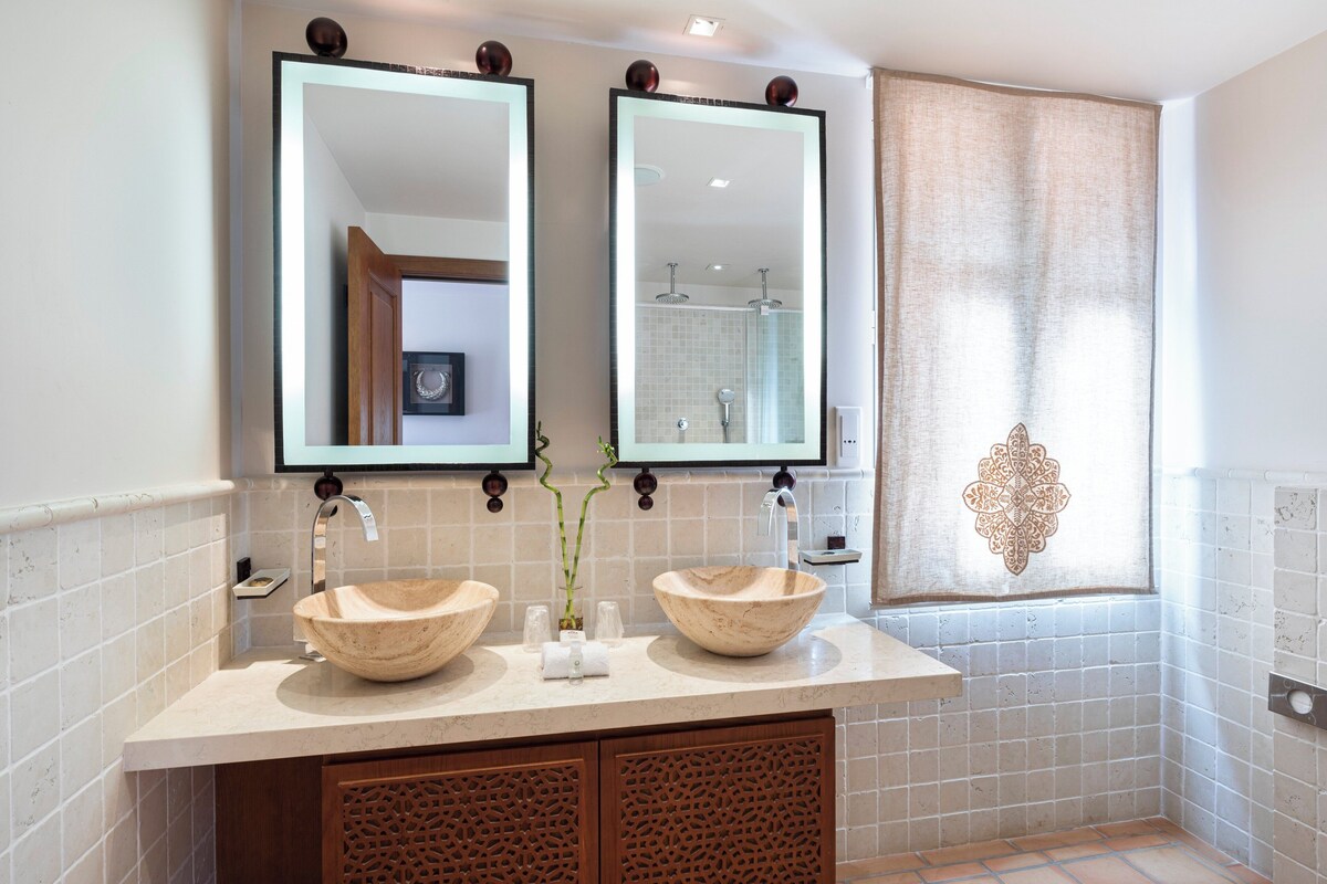 A bathroom with two large, round sinks, a double mirror, and a decorative tile pattern on the wall.