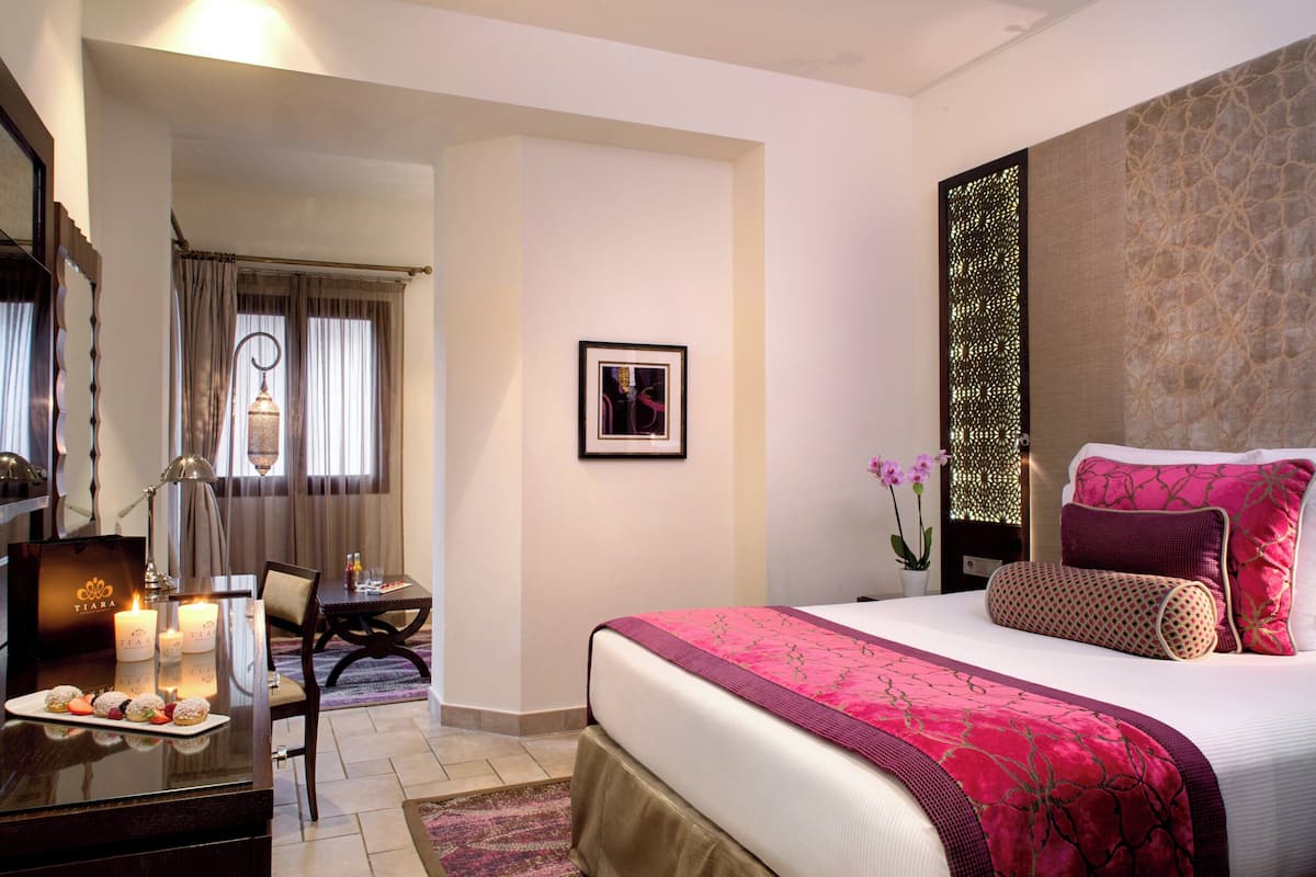 A hotel room with a large bed, a desk with a lamp, a dining table, and a decorative wall.