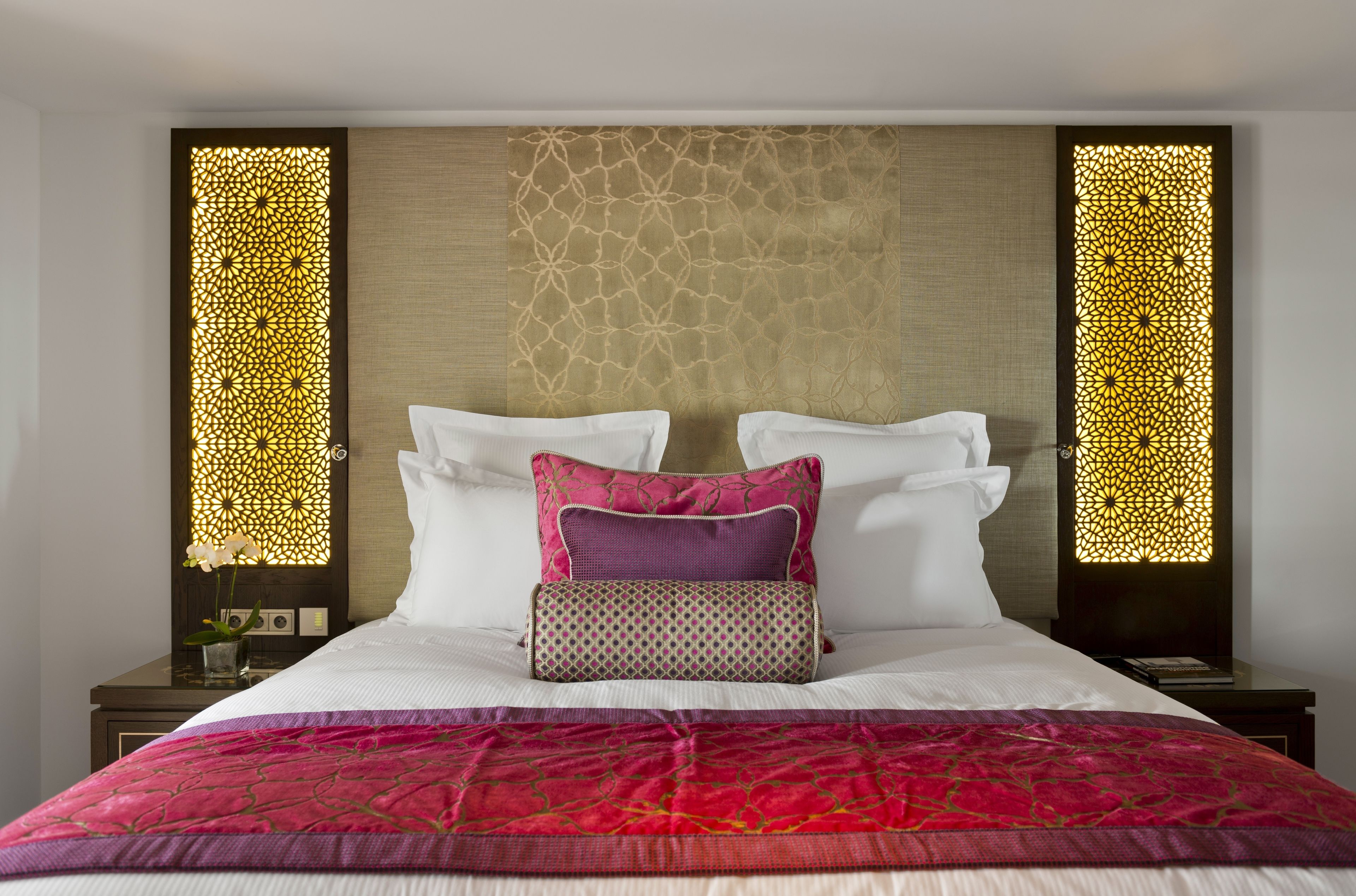 Un letto rifatto con cuscini bianchi e rosa, una coperta decorata e un pannello ornamentale a parete.