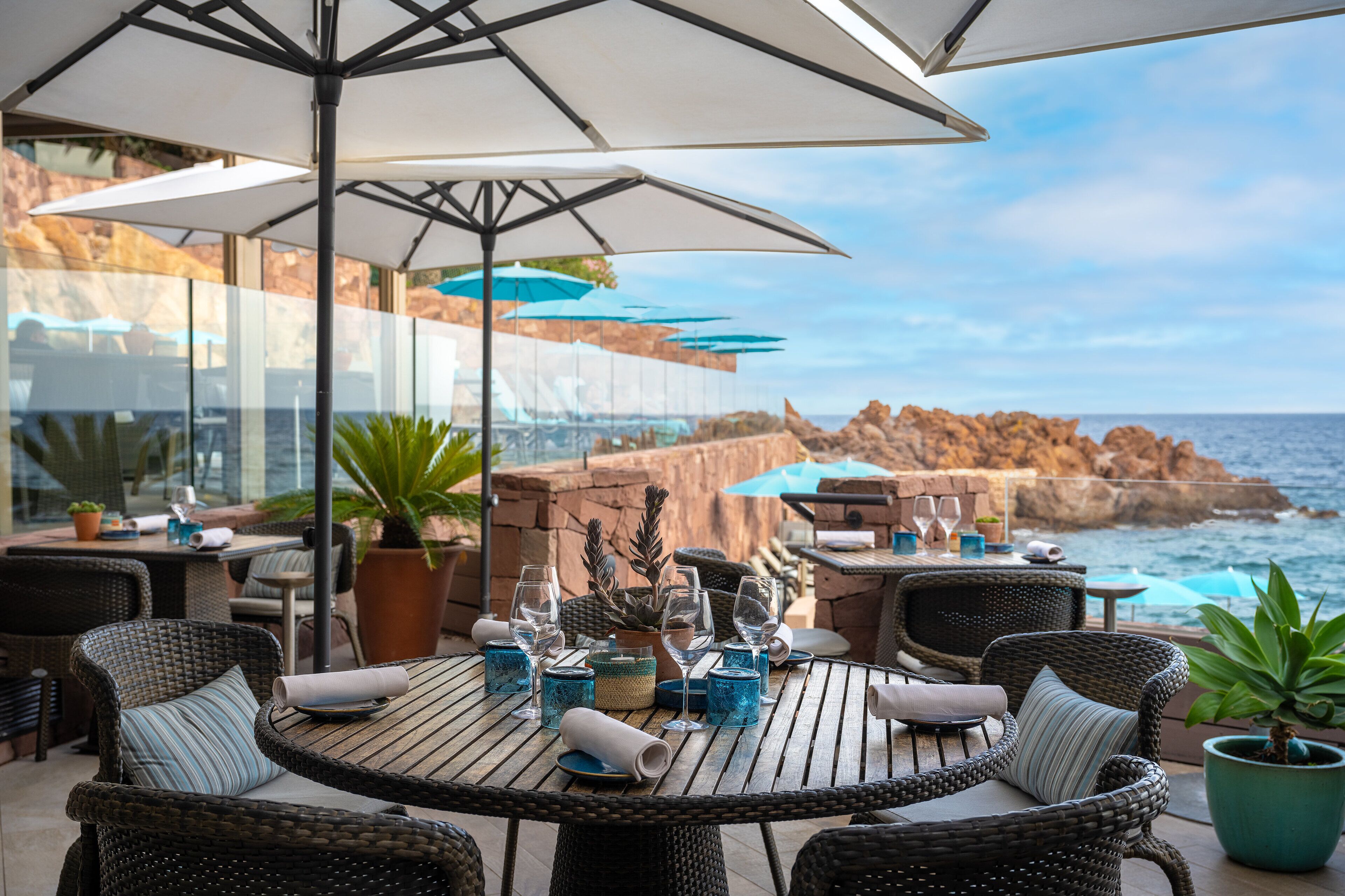 An outdoor dining area with wicker furniture, umbrellas, and potted plants.