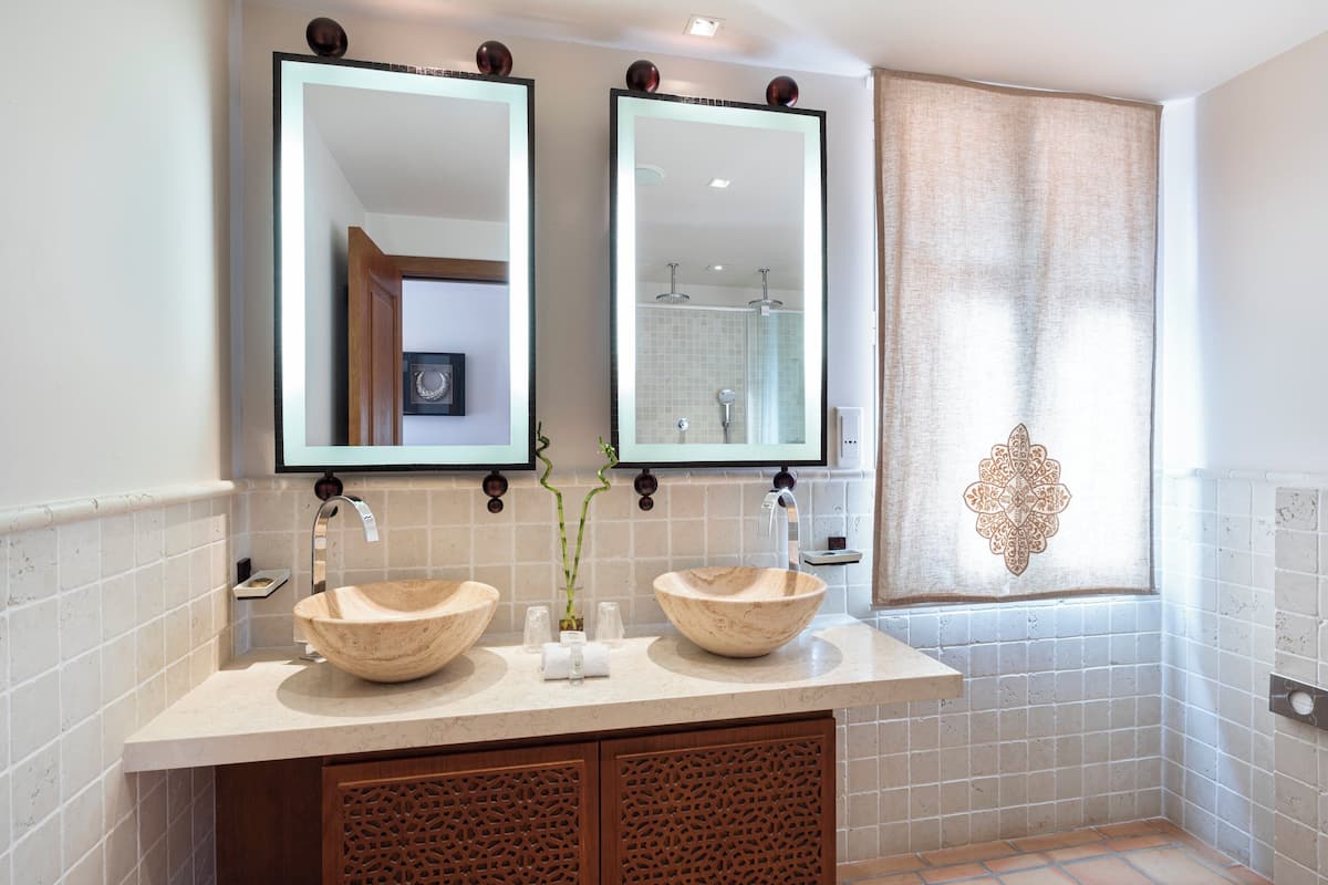 Un baño con dos lavamanos grandes y redondos, un espejo doble y un diseño decorativo de azulejos en la pared.