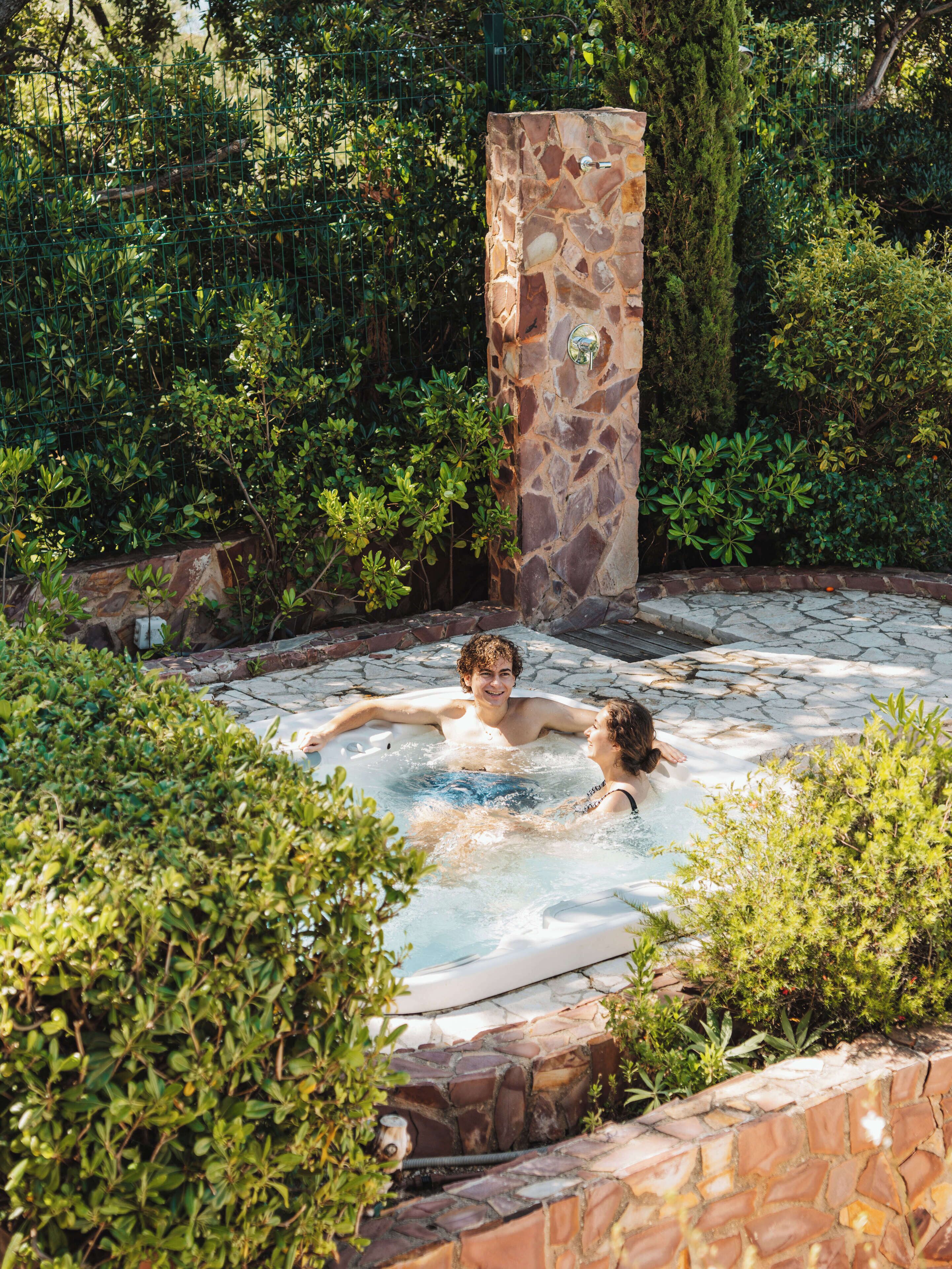 Un bain à remous dans un jardin agrémenté de murs en pierre et d’une végétation luxuriante.
