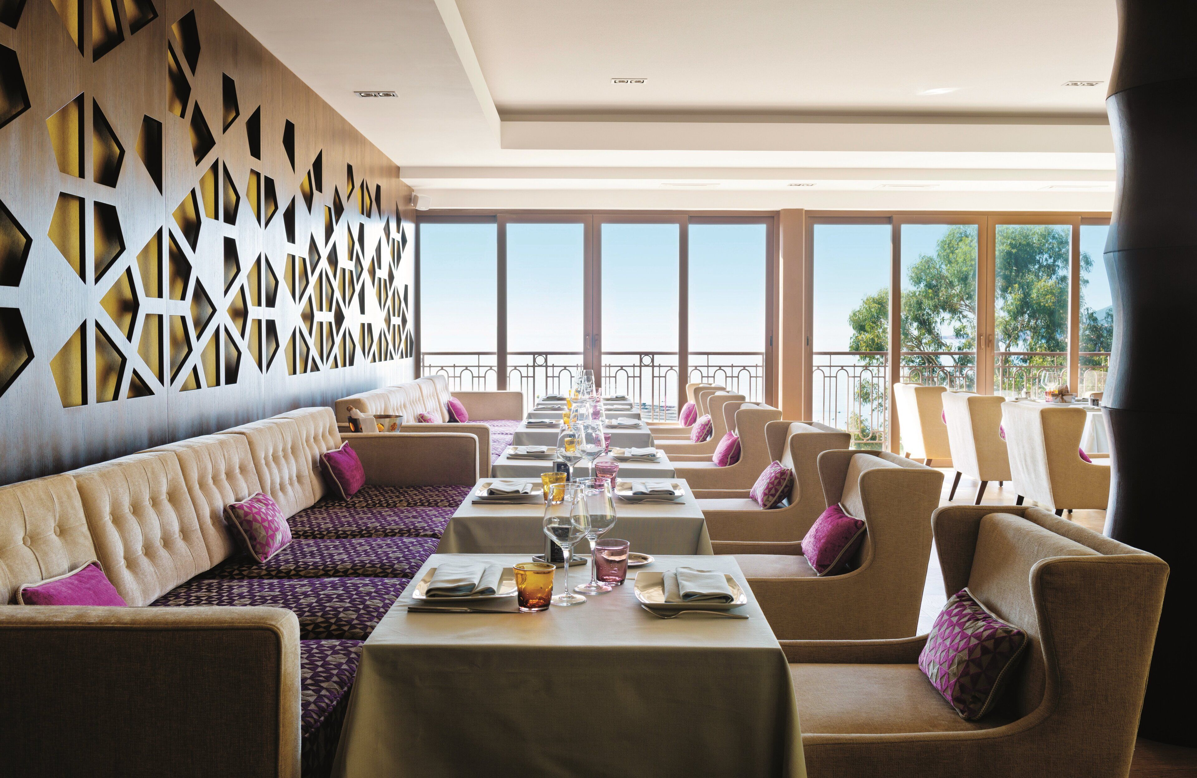 A restaurant with a long dining area, cushioned seating, and large windows offering a view of the outdoors.