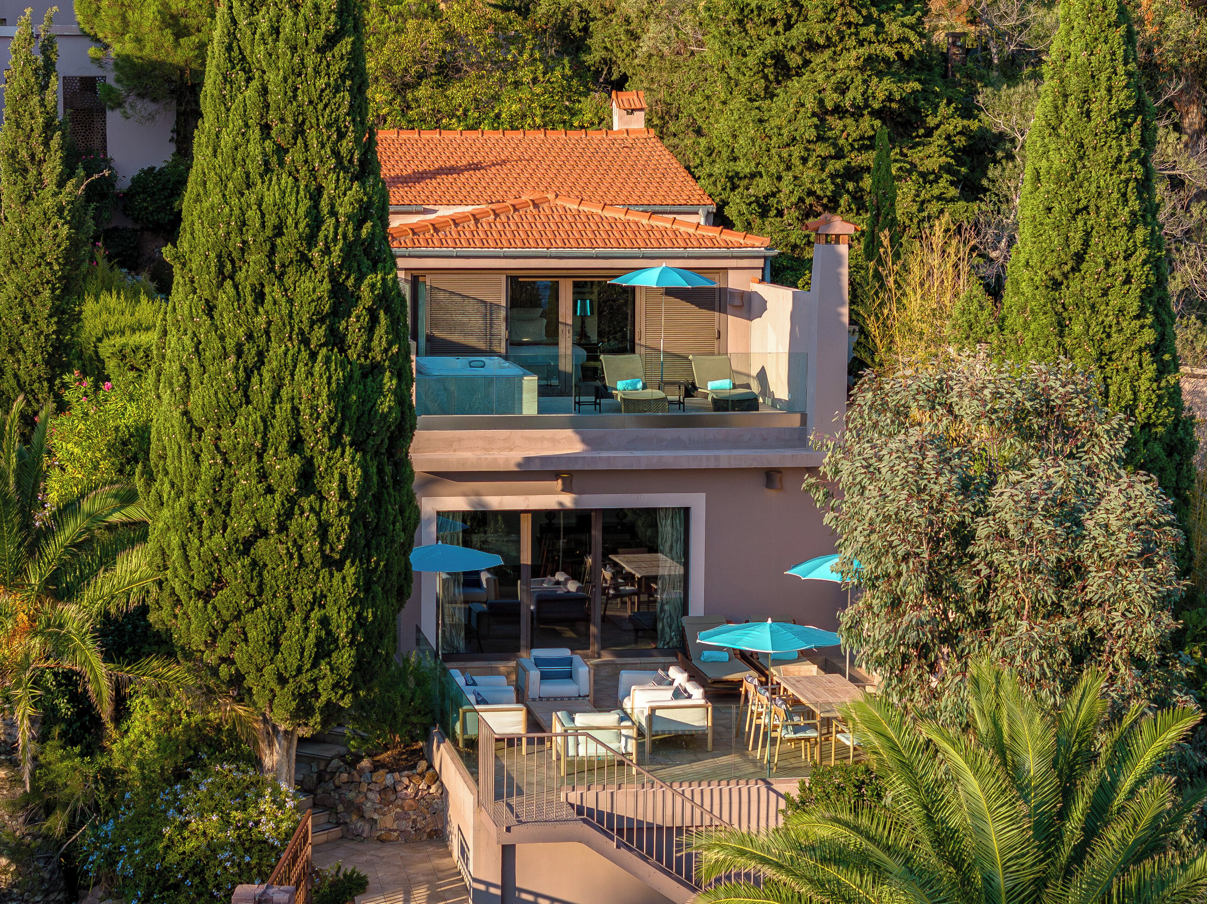 A two-story house with a balcony, outdoor seating, and a view of surrounding trees.