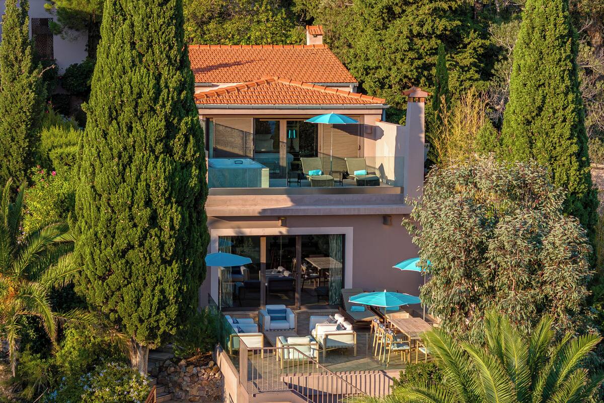 Una casa de dos pisos con balcón, mobiliario exterior y vistas a árboles circundantes.