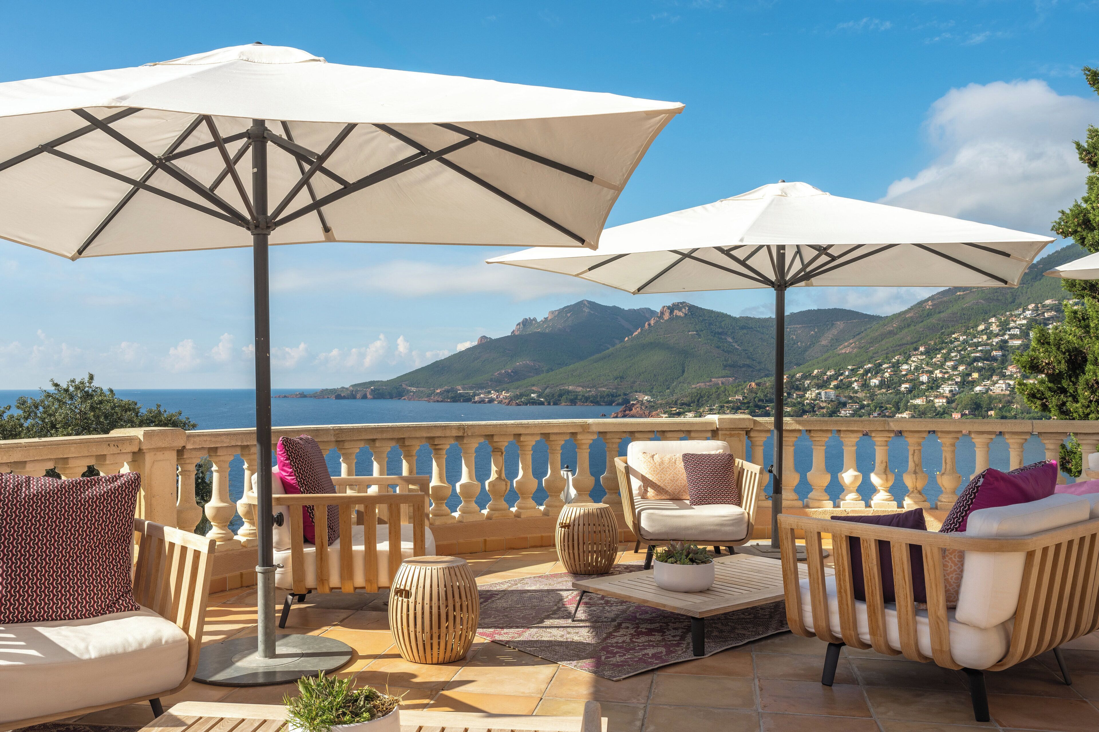 Une terrasse avec des places assises extérieures, des parasols et une vue panoramique sur la mer et les montagnes.
