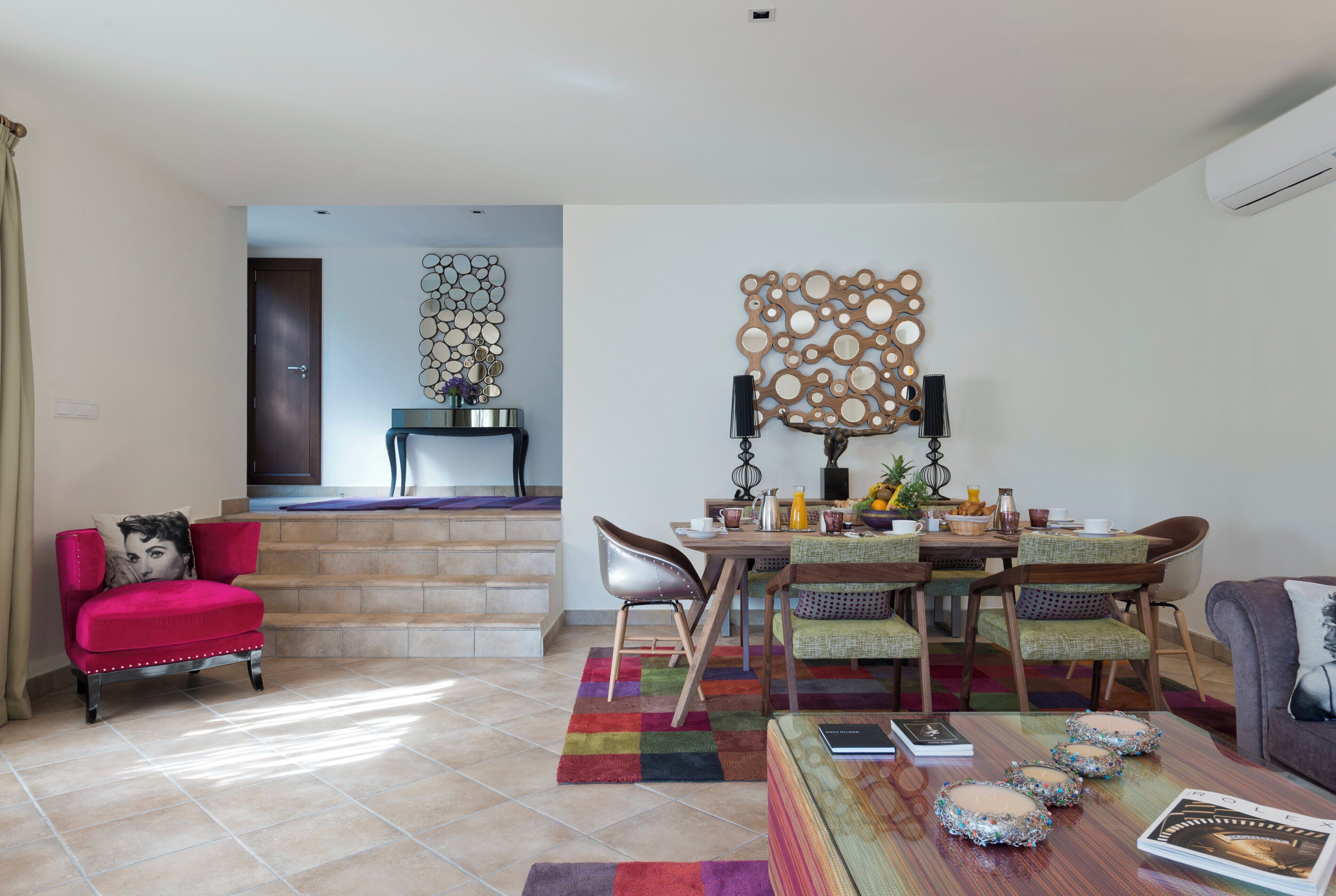 Un amplio espacio de estar con un sillón rojo, una mesa de comedor con sillas y una alfombra colorida.