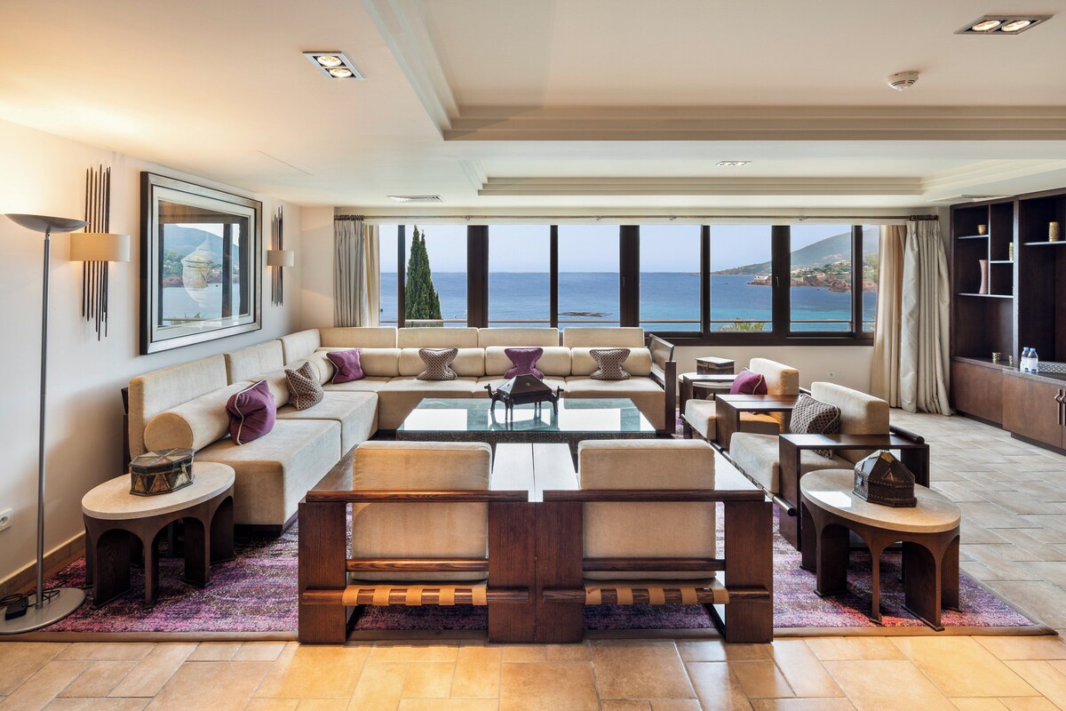 A spacious living room with a large sectional sofa, a coffee table, and a view of the sea.