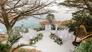 An outdoor wedding venue with a white aisle, floral decorations, and a harp. - Tiara Miramar Beach Resort (Theoule-sur-Mer)