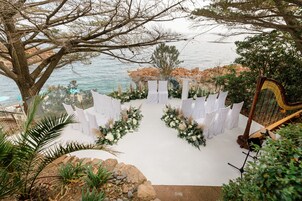 Un salón de bodas al aire libre con un pasillo blanco, decoración floral y un arpa.