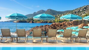 A poolside area with lounge chairs and umbrellas, overlooking a coastal landscape with houses and mountains. - Tiara Miramar Beach Resort (Theoule-sur-Mer)