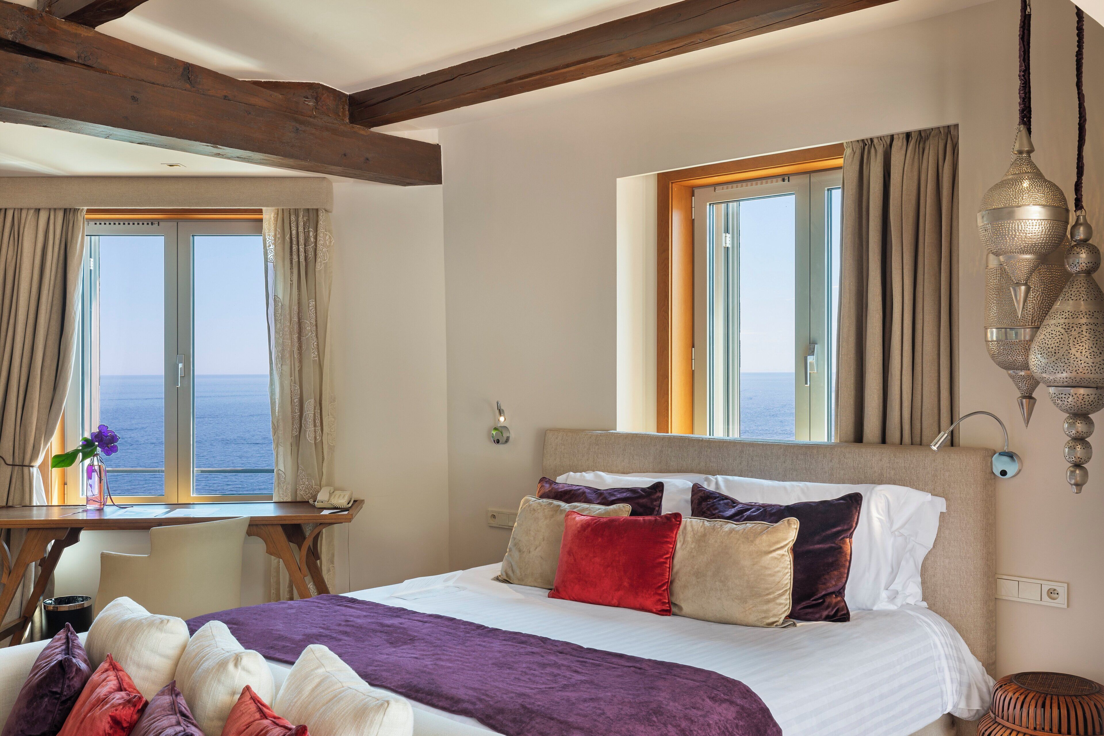 A bedroom with a large bed, a desk, and a view of the sea.