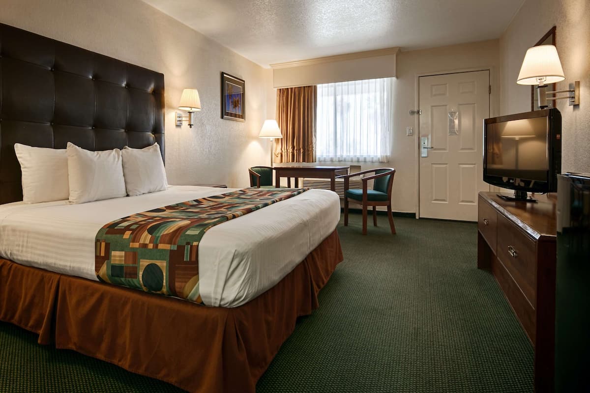A hotel room with a large bed, a desk, a television, and a chair.