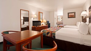 A hotel room with a bed, a desk, a chair, a television, a lamp, and a mirror.