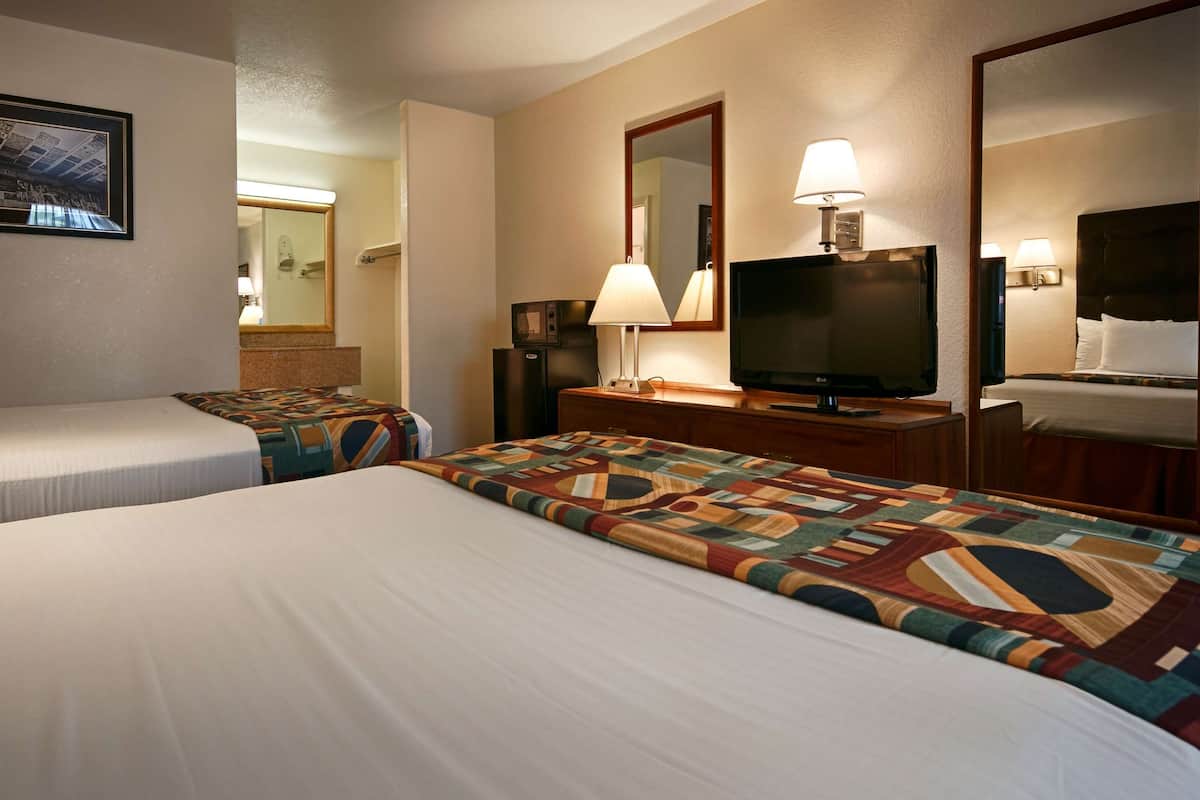 A hotel room with two beds, a television, a mirror, and a framed picture on the wall.