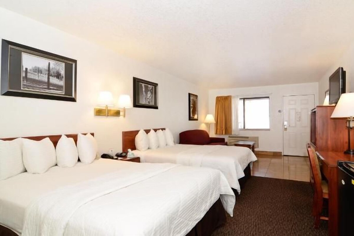 Une chambre d’hôtel avec deux lits, un bureau, une chaise, une télévision et une fenêtre.
