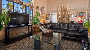 A living room with a black leather sofa, a glass coffee table, and a TV on a black stand. There are potted plants, a lamp, and Route 66 memorabilia on the walls.