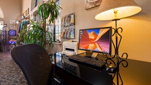 A hotel room with a desk, computer, and a lamp. There are plants and decorations on the wall.