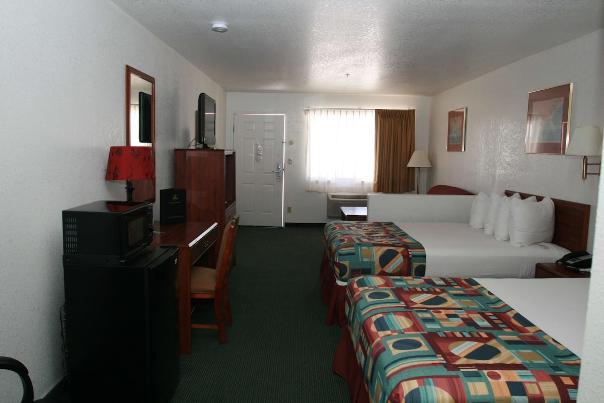 A hotel room with two beds, a desk with a computer, a microwave, and a television.