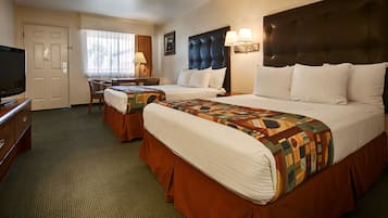 A hotel room with two beds, a desk, a television, and a window with curtains.