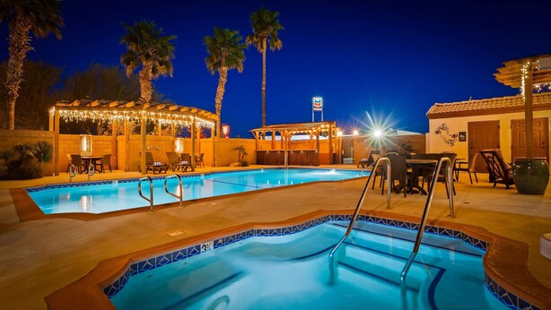 A swimming pool with lounge chairs and a covered seating area, surrounded by palm trees and a Chevron sign.