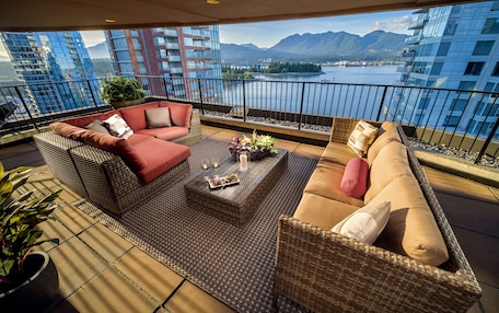 A balcony with wicker furniture, a view of a lake, and mountains in the background.